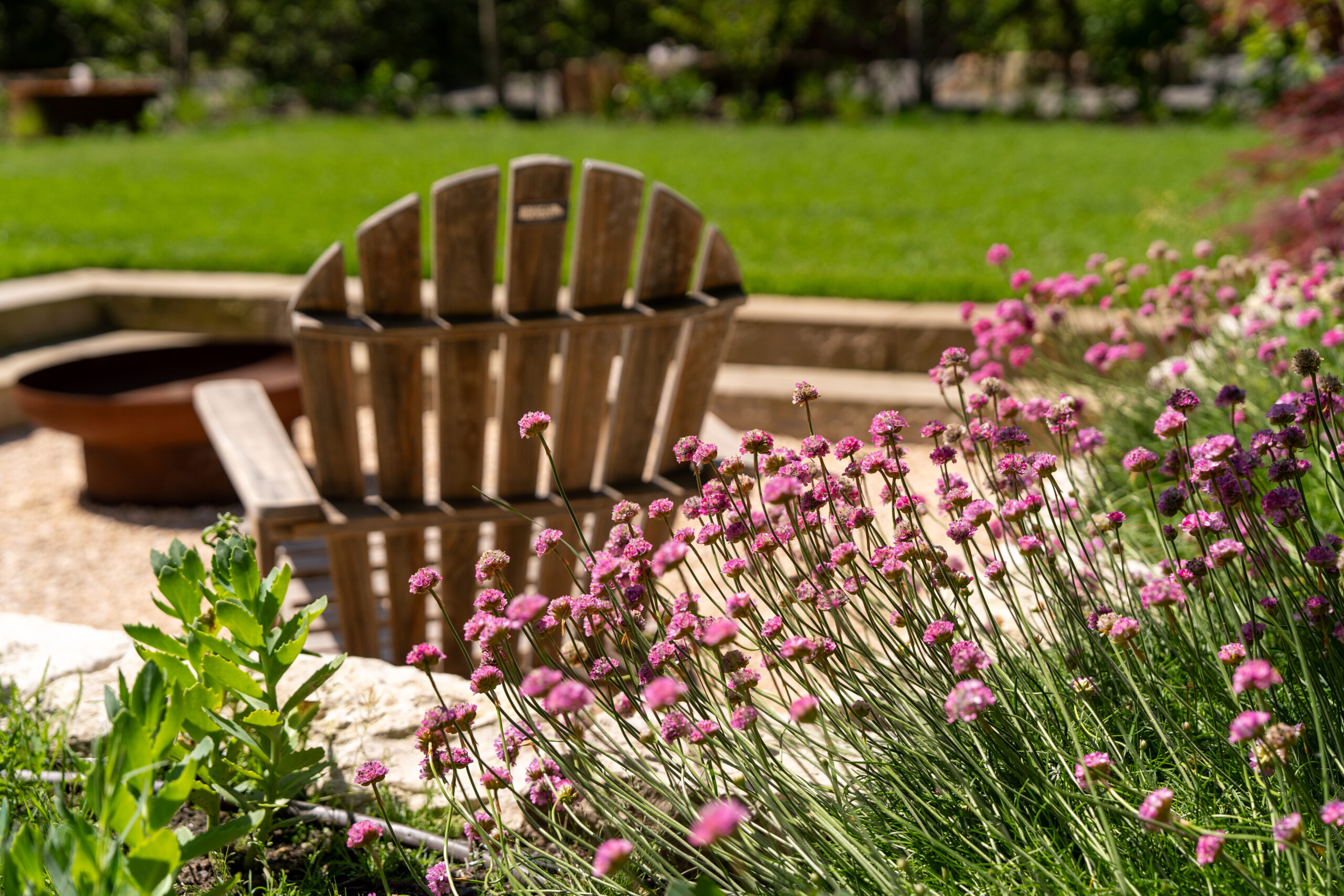 Gestalteter Gartensitzplatz mit Holzsessel, Naturstein und blühenden Stauden